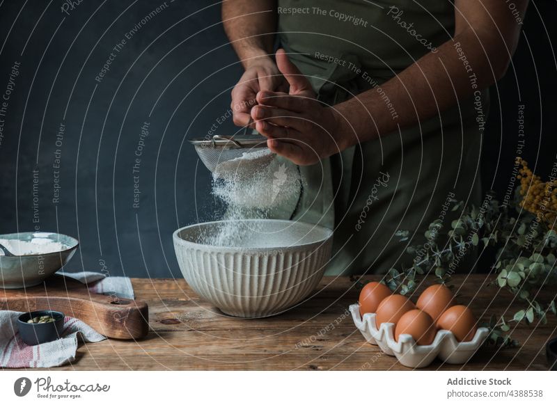 Anonymer Mann beim Backen von Gebäck sieben Mehl Küche Sieb Schalen & Schüsseln Lebensmittel Bestandteil Prozess Pulver Utensil Tisch vorbereiten organisch