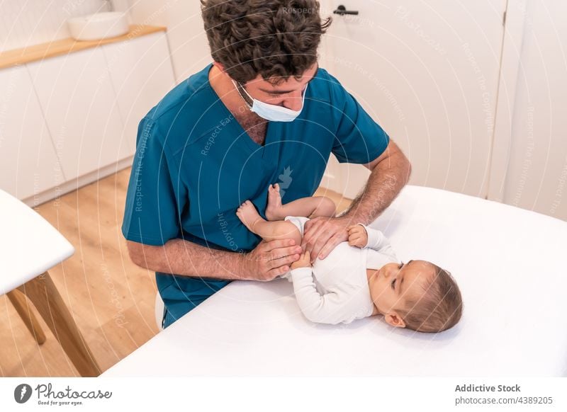 Männlicher Kinderarzt, der ein süßes Baby auf einem medizinischen Tisch in einer Klinik untersucht Kinderärztin Arzt Säugling untersuchen Diagnostik besuchen