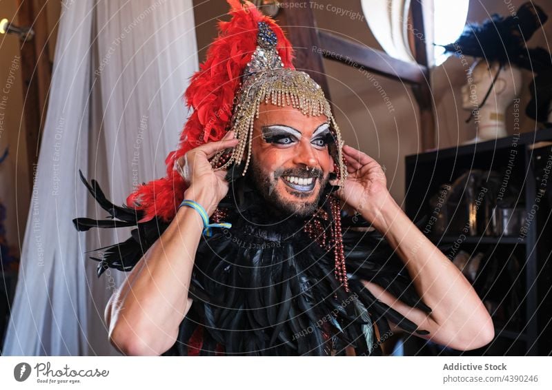 Bärtiger Mann im Drag-Queen-Kostüm Drag Queen Make-up Outfit Kopfschmuck Lächeln anhaben Geschlecht Tracht Accessoire Feder Kleid Kopfbedeckung Armband Stolz