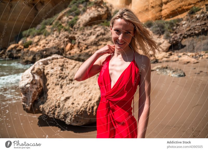 Charmante glückliche Frau im roten Kleid am Strand Stil Sommer Mode Farbe Charme provokant jung blond Outfit Aussehen Sonnenkleid Dekolleté nackte Schultern