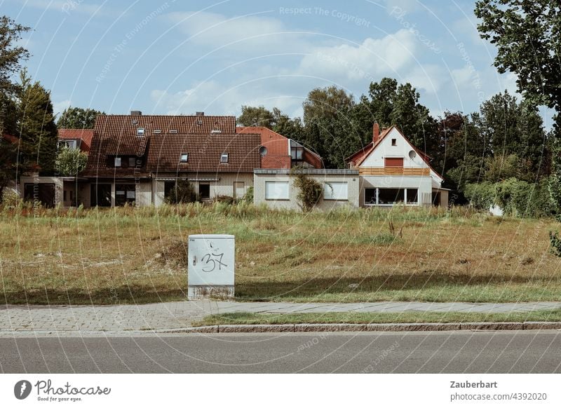 Straße, Wiese mit Verteilerkasten, Fassaden von Einfamilienhäusern, Kleinstadt Baulücke Vergänglichkeit Häuser Bürgersteig trist Tristesse menschenleer