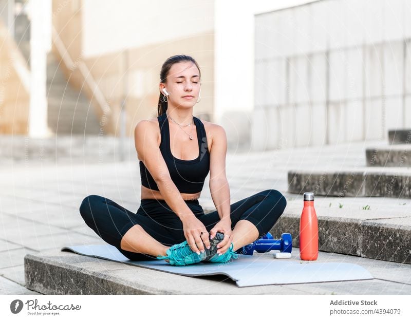 Junge Sportlerin beim Stretching auf der Straße Dehnung Übung Fitness Training Schritt Aufwärmen zuhören Musik Frau jung Wegbiegung passen Athlet Kopfhörer tws