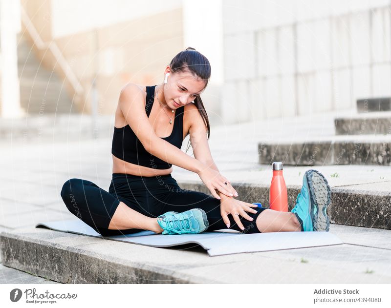 Junge Sportlerin beim Stretching auf der Straße Dehnung Übung Fitness Training Schritt Aufwärmen zuhören Musik Frau jung Wegbiegung passen Athlet Kopfhörer tws