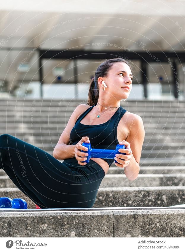 Weibliche Athletin beim Training mit Hantel auf Stufen Sportlerin Übung Bauchmuskeln Schritt Fitness Kurzhantel Straße zuhören Musik Frau jung verdrehen