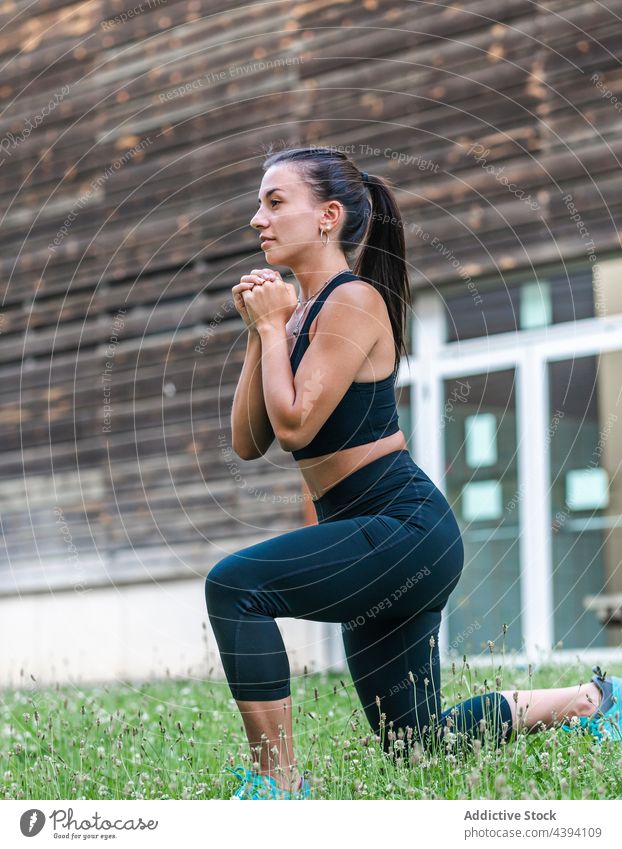 Weibliche Athletin beim Longieren auf Rasen Sportlerin Ausfallschritt Training Fitness Hof Übung passen Wellness Sommer Frau Gras jung Hände gefaltet Vitalität