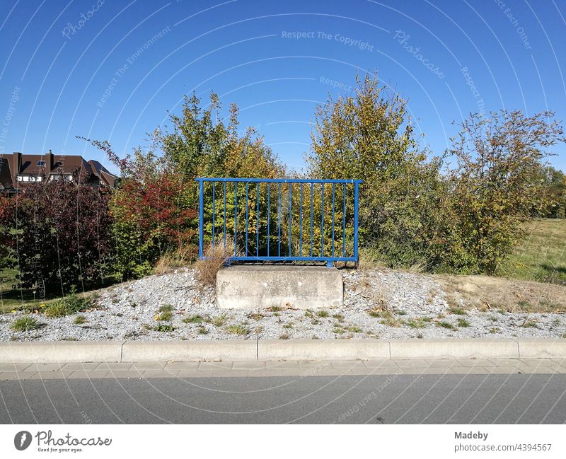 Einsames blaues Geländer aus Stahl mit Fundament aus Beton allein auf weiter Flur vor blauem Himmel bei Sonnenschein in Oelde bei Warendorf in Westfalen im Münsterland