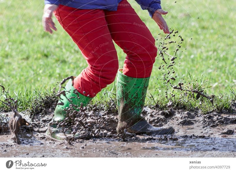 Mit grünen Gummistiefel und roter Hose in den Matsch springen macht Spaß spritzen dreckig kleckern Freude Pfütze Spielen Herbst Schlamm braun Kindheit Jeanshose