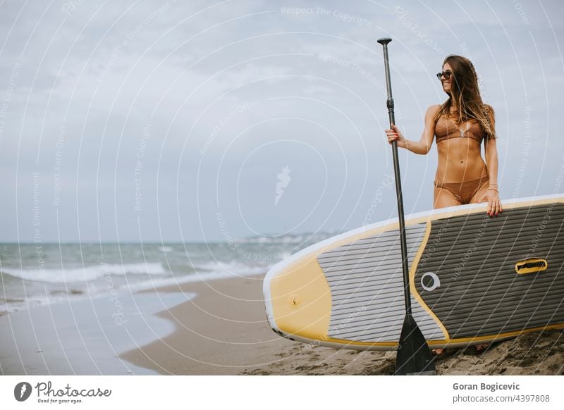 Junge Frauen mit Paddelbrett am Strand an einem Sommertag attraktiv schön Bikini Holzplatte Küste Tag passen Spaß Glück Lifestyle Meer im Freien Menschen Person