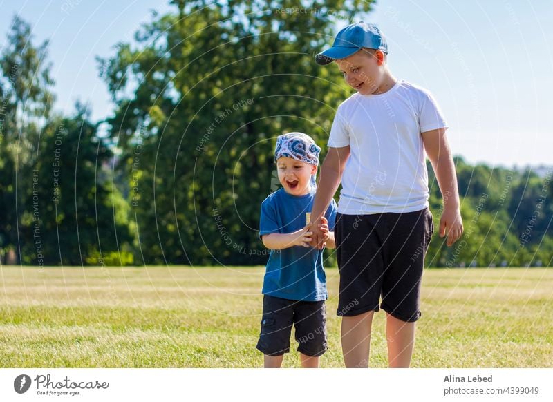 Fröhliche Kinder, zwei Brüder, lächeln vor Freude. Wir sind glücklich zu gehen und spielen auf dem Rasen in warmen sonnigen Wetter im Park. die Emotionen der Kinder auf dem Gesicht.