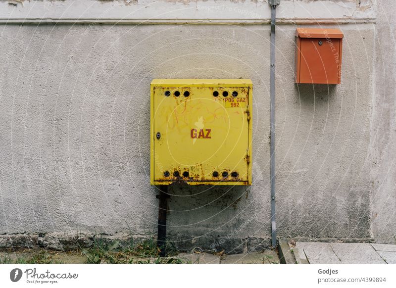 Gelber Gasanschluss-Kasten und oranger Briefkasten an einer Betonwand Gaz Wand Mauer Menschenleer Fassade Post Tag Farbfoto Außenaufnahme alt Häusliches Leben