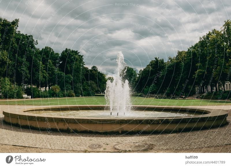 runder Springbrunnen im Park Wasserfontäne Brunnen Wassertropfen Wasserfontänen Wolken Wolkenhimmel spritzen Sonnenlicht nass frisch Bewegung sprudelnd kalt