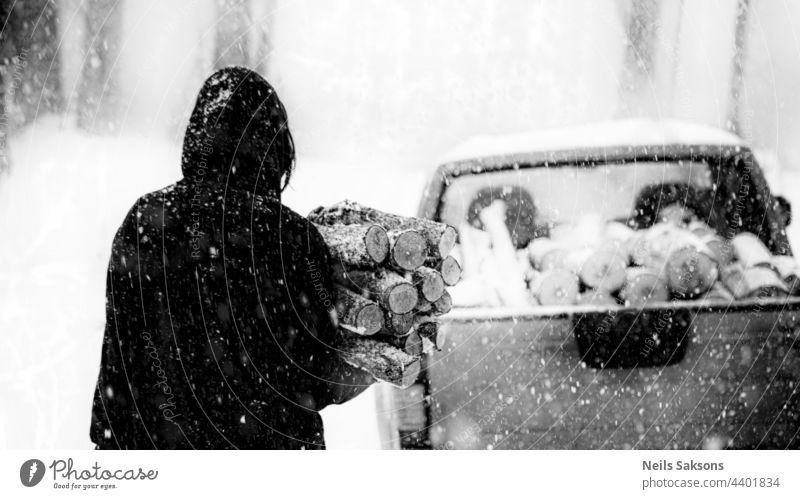 Silhouette des Mannes mit geschnittenem Brennholz im Wald, Nahaufnahme, rohe weiße Erle Brennholz in Schneefall Wintertag, Vorbereitung Holz für das nächste Jahr. Snowy kalten Januar oder Februar Abend. Menschen arbeiten mit den Händen