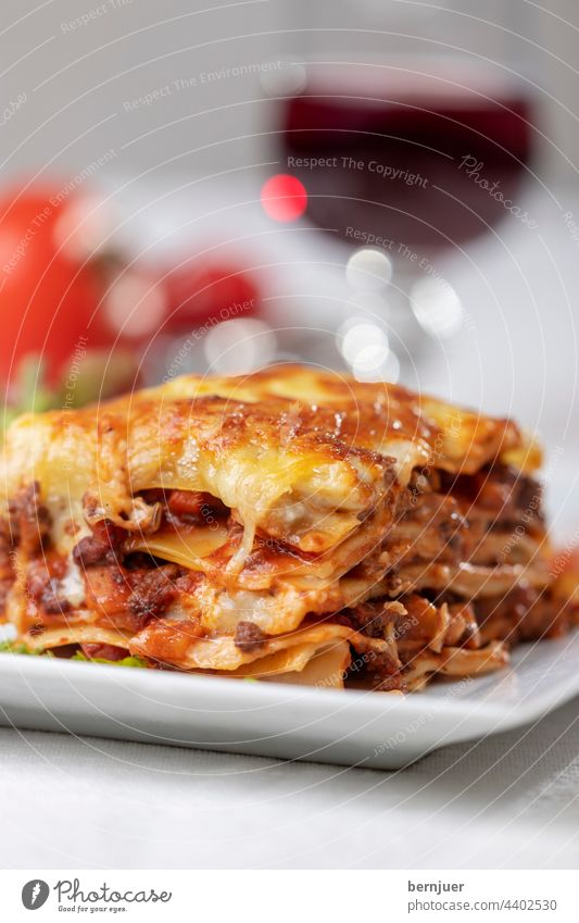 Portion Lasagne auf einem Teller Tomate Rot Wein Glas Salat Essen Sauce Basilikum Pasta Italienisch Fleisch Rindfleisch Bolognese Käse frisch gebacken