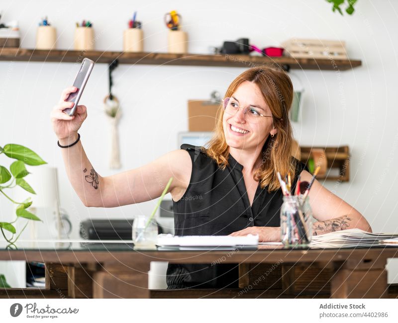 Lächelnde Künstlerin macht Selfie im Kreativstudio Frau Designer heiter Selbstportrait Smartphone Anstreicher Werkstatt benutzend Apparatur Gerät fotografieren