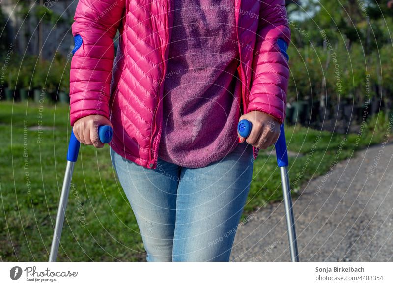 Frau mit Krücken nach Sportverletzung Gehhilfe Wintersport Mensch Außenaufnahme Spaziergang Farbfoto Gesundheit laufen gehen Bewegung Fußgänger Beine Straße