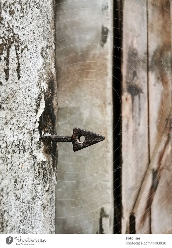 Lost Place - aus einer alten Wand ragt ein schmiedeeiserner Pfeil. Mauer Menschenleer Spitze Loch dreieckig rund richtungsweisend Schwache Tiefenschärfe grau