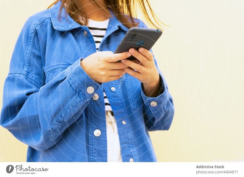 Anonyme Frau, die ihr Smartphone gegen eine Wand in der Stadt hält benutzend trendy Stil Großstadt Surfen Browsen Nachricht Funktelefon Straße Outfit urban jung