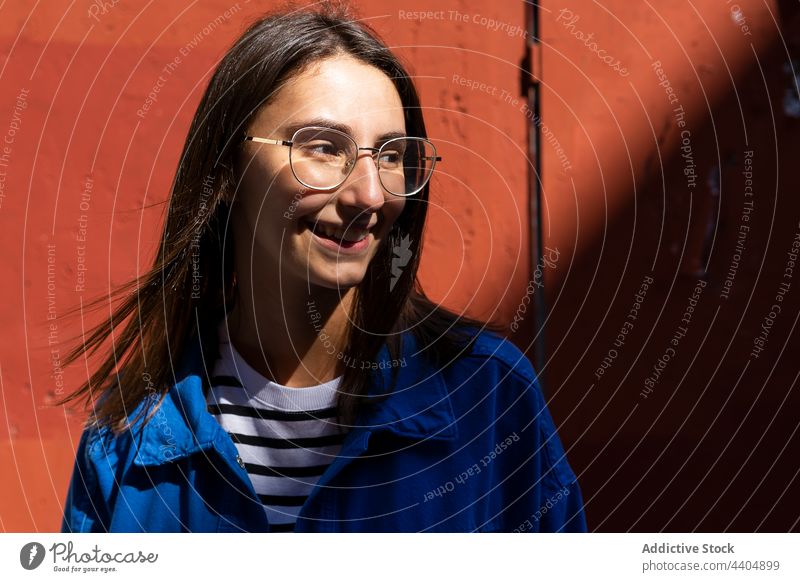 Glückliche Frau lächelt an einem sonnigen Tag in der Stadt heiter Freude Stil urban Straße Großstadt Gebäude Wand Lächeln trendy Outfit farbenfroh Brille