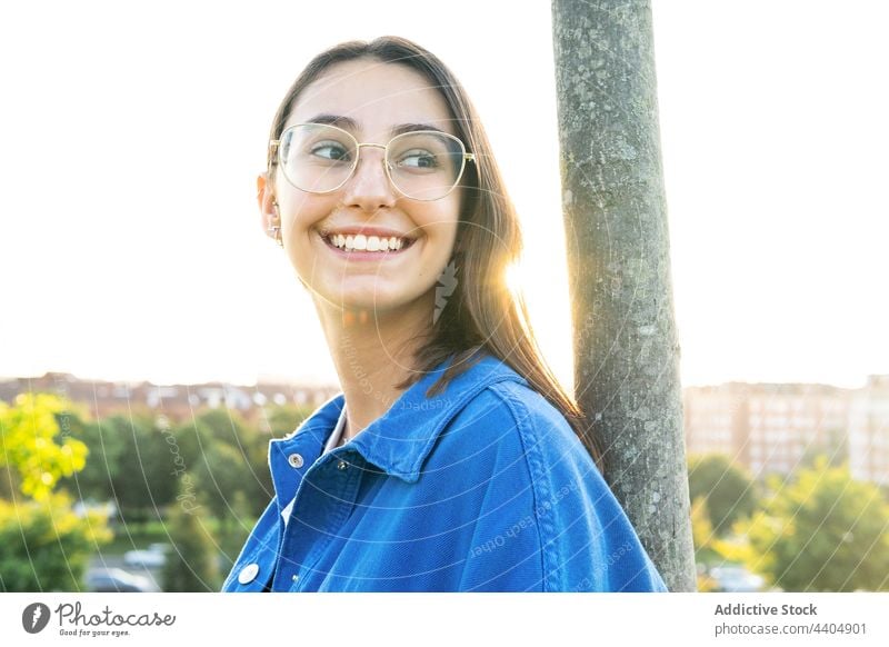 Glückliche Frau steht in der Nähe eines Baumes auf einem Hügel in der Stadt fettarm Kofferraum Gelassenheit Großstadt natürlich trendy Stil Windstille stehen