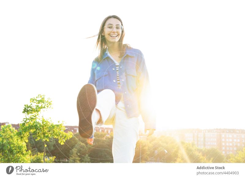 Erfreute Frau streckt das Bein in die Kamera Kick ausdehnen heiter Großstadt Spaß haben Lächeln urban sonnig Stil trendy Outfit positiv Freude charmant cool