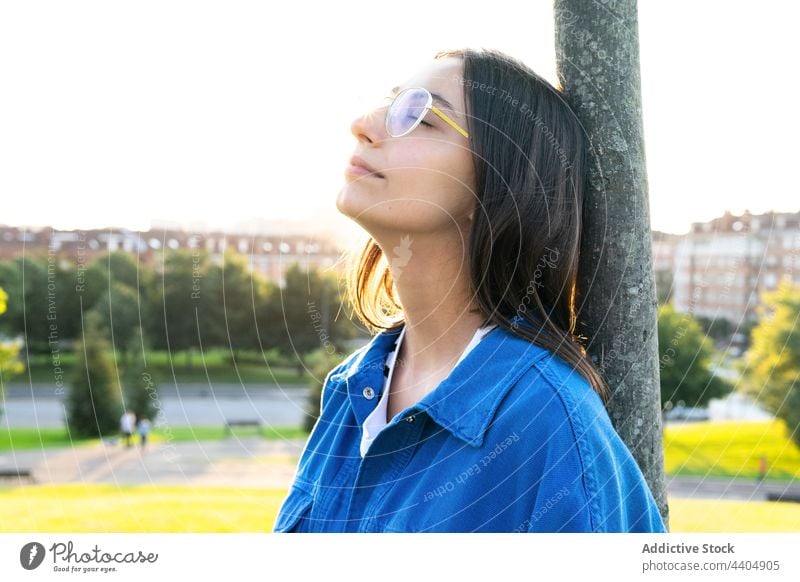 Ruhige Frau steht in der Nähe von Baum auf Hügel in der Stadt fettarm Kofferraum Gelassenheit Großstadt natürlich Harmonie friedlich trendy Stil Windstille