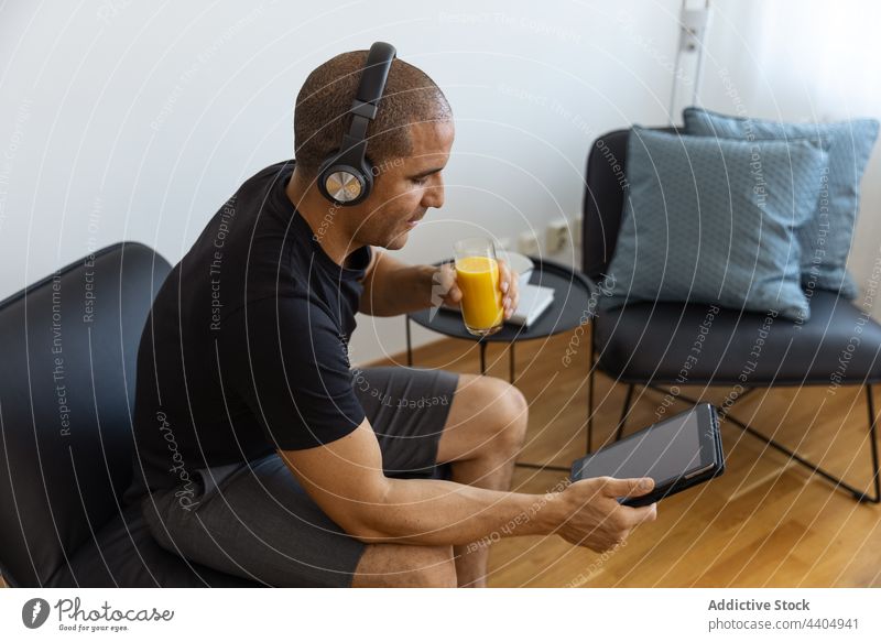 Zufriedener Mann, der zu Hause Saft trinkt und eine Tablette benutzt zuschauen benutzend Video trinken orange heimwärts Morgen männlich Browsen Surfen sitzen