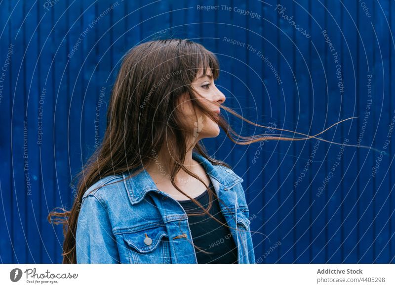 Gelassene Frau mit fliegenden Haaren auf blauem Hintergrund fliegendes Haar lange Haare Gelassenheit Farbe Stil braune Haare ruhig Großstadt urban friedlich