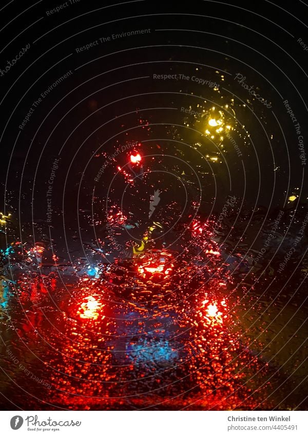 Blick durch die regennasse Windschutzscheibe auf beleuchtete Autos, die in der Dunkelheit an einer Ampel warten Regen Lichter im Regen Autolichter verregnet