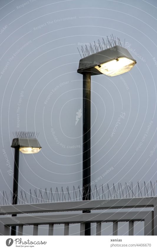 Vögel unerwünscht - Zwei leuchtende Laternen mit Stachel vor Gitter und grauem Himmel bei Dämmerung Lampe Straßenbeleuchtung Vogelabwehr Licht Pickser zwei