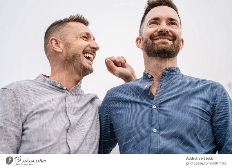 Fröhliches Schwulenpaar im Gespräch unter hellem Himmel Paar lgbt Lachen interagieren Zeit verbringen Partnerschaft romantisch offen Männer gleichgeschlechtlich