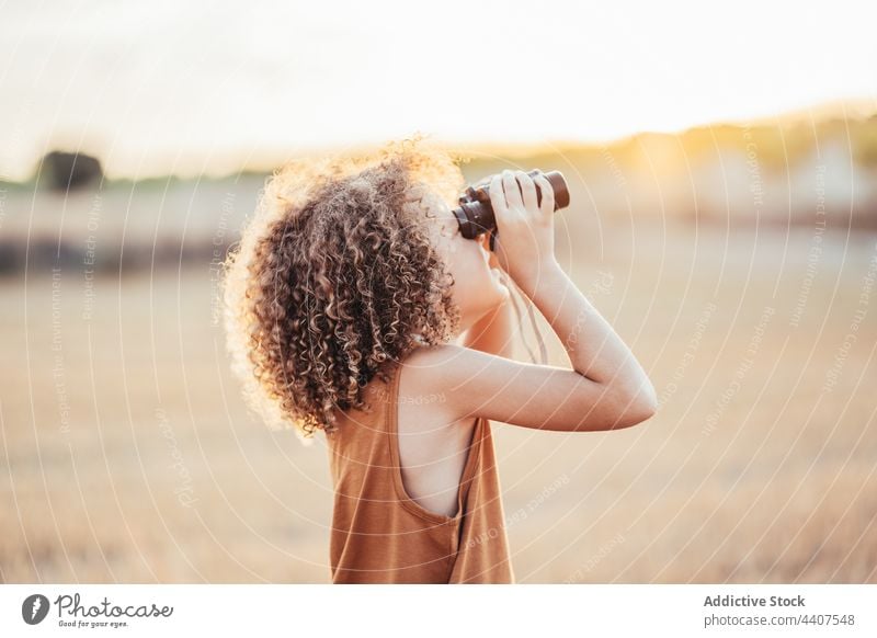 Glückliches ethnisches Kind, das durch ein Fernglas in einem Feld im Sommer schaut spielen Spiel feiern Sieg heiter aufgeregt genießen Spaß haben Freude