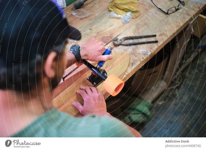 Fokussierter Handwerker, der in einer leichten Werkstatt ein Skateboard herstellt Kunstgewerbler Rad befestigen professionell handgefertigt Talent Mann machen