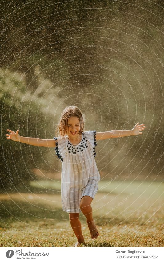 Niedliches kleines Mädchen hat Spaß unter Bewässerung Sprinkler Glück Kind Sommer Fröhlichkeit Freude Sprinkleranlage Spray nass aktiv Wasser im Freien