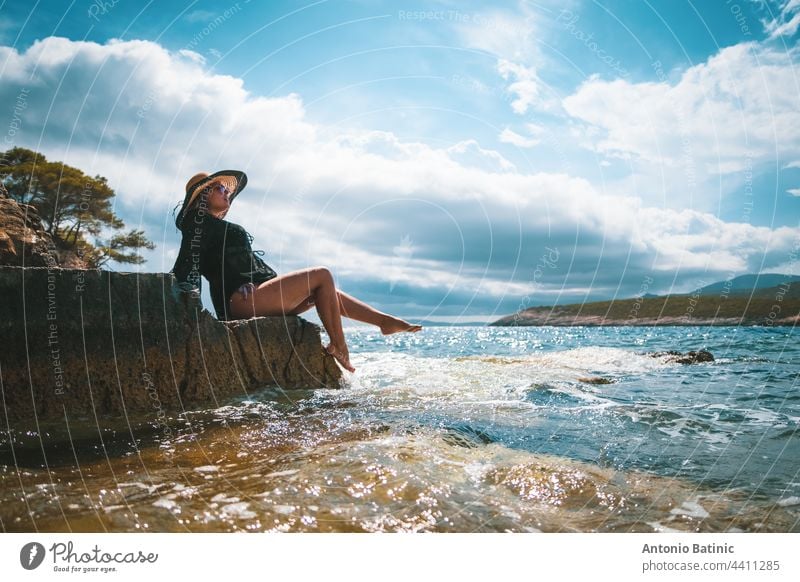 Erstaunlich Blick auf eine Brünette sitzt auf einem Felsen in der Nähe des Meeres. Erstaunliche Sommerwetter in Kroatien, vis Insel. Sonnenbaden in der Sonne mit Wellen, die an das Ufer schlagen