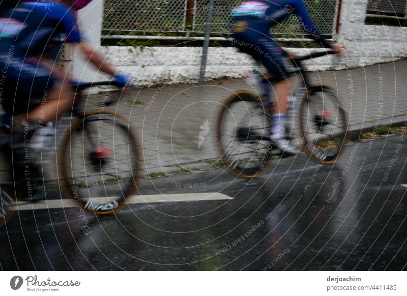 Zwei Radrennfahrer treten voll in die Pedale, kurz bevor sie  einen Anstieg  erreichen . Sie sind beide unscharf. radfahrer Fahrrad Fahrradfahren Straße