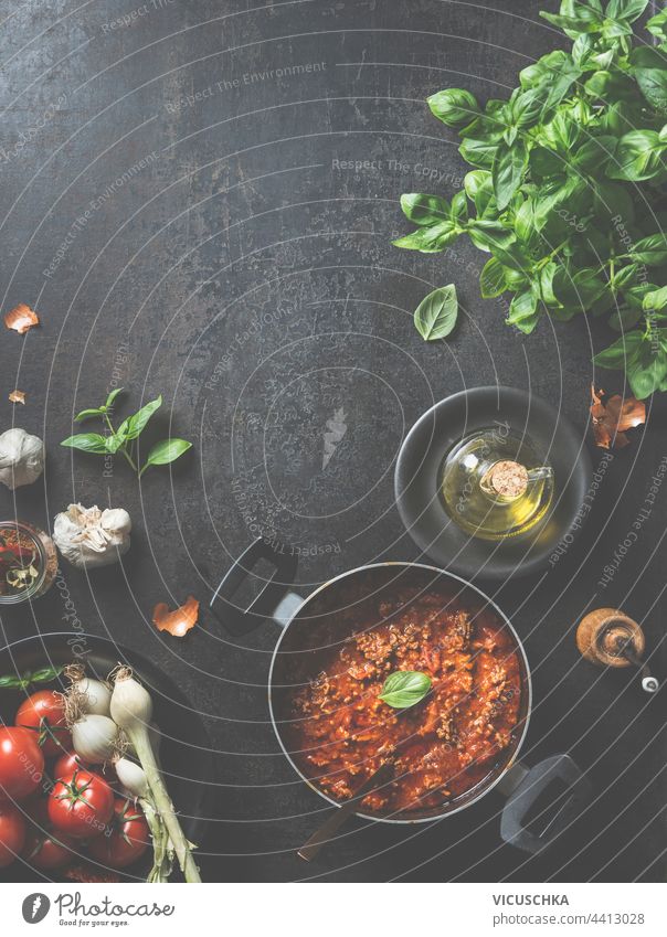 Köstliche Sauce Bolognese, zu Hause in einer schwarzen Pfanne mit Löffel und Basilikumblättern auf dem dunklen Küchentisch mit frischen Zutaten und Olivenöl zubereitet. Blick von oben. Rahmen. Lebensmittel Hintergrund