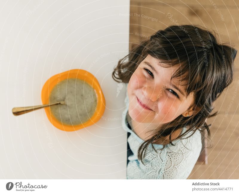 Fröhliches Mädchen sitzt mit Suppe am Tisch beim Mittagessen Kind Küche Lebensmittel Mahlzeit Schalen & Schüsseln Sahne Püree heiter Kindheit niedlich heimisch