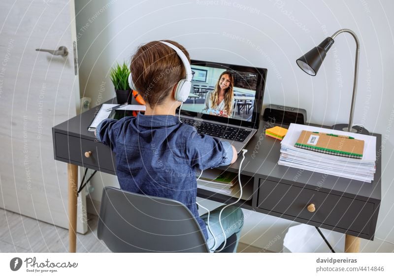 Unbekannter Junge mit Kopfhörern, der zu Hause mit einem Laptop aus seinem Schlafzimmer Unterricht erhält unkenntlich hören Lehrer Schule zu Hause Videoanruf