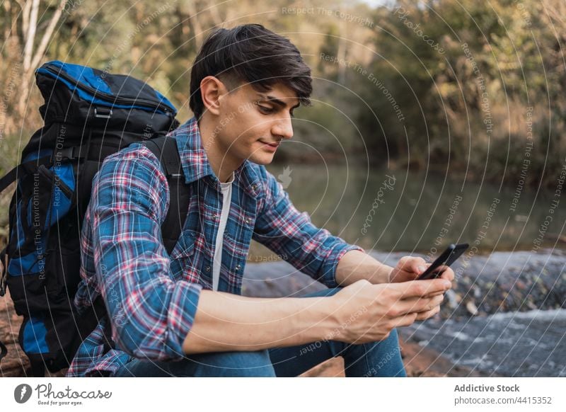 Lächelnder Reisender mit Smartphone während einer Wanderung Mann Browsen Rucksack Trekking Wald benutzend Wanderer reisen männlich Natur Apparatur Inhalt Gerät