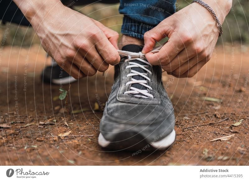 Crop Reisende binden Schnürsenkel der Turnschuhe im Wald Reisender Krawatte Schuhbänder Spitze Schuhe Wanderer Trekking Mann männlich Wälder Natur Sport Stil