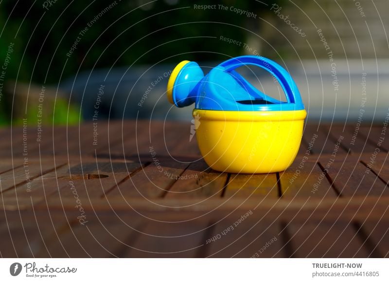 Bunte Gießkanne. Wartet auf dem Gartentisch. Auf Kinderhände. Holz Kindergießkanne bunt blaugelb Plastik Kunststoff Kinderspielzeug nützlich