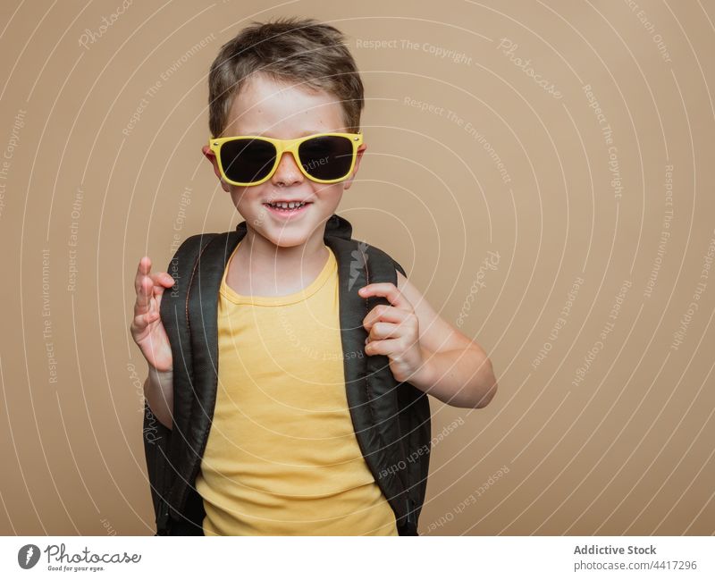 Lächelnde Schülerin mit Rucksack und Sonnenbrille im Studio Pupille Kind Junge cool Atelier Schuljunge Schulkind heiter Glück positiv Kindheit froh Optimist