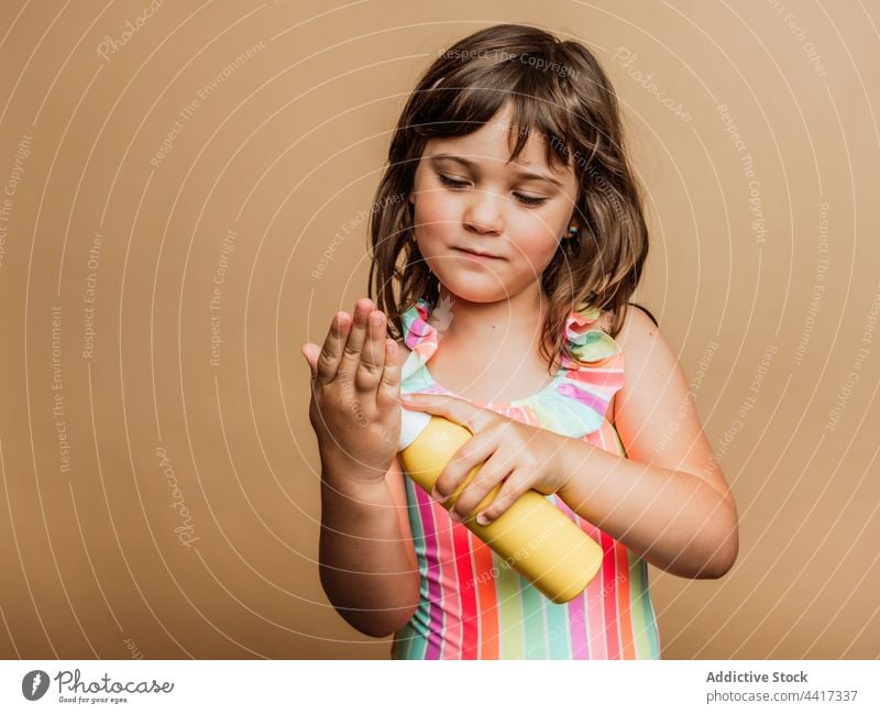 Lächelndes Mädchen im Badeanzug trägt im Studio Sonnenschutzcreme auf die Hand auf Kind bewerben Sonnencreme Sahne Lotion Sommer Bräune Badebekleidung