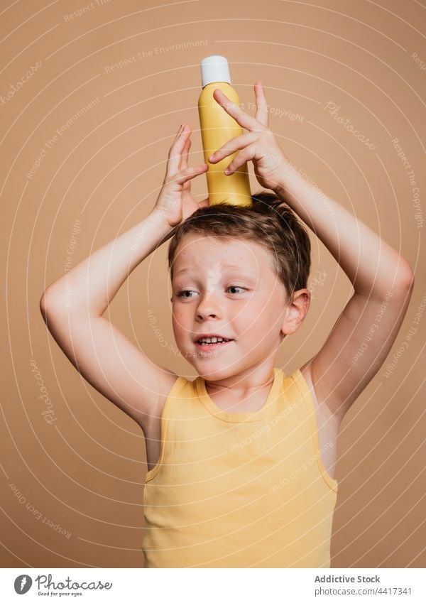 Lustiges Kind mit Sonnenmilch auf dem Kopf im Studio Sonnenschutz Lotion Junge Sonnencreme Sahne Badeanzug lustig Gleichgewicht Spaß haben Sommer Bräune