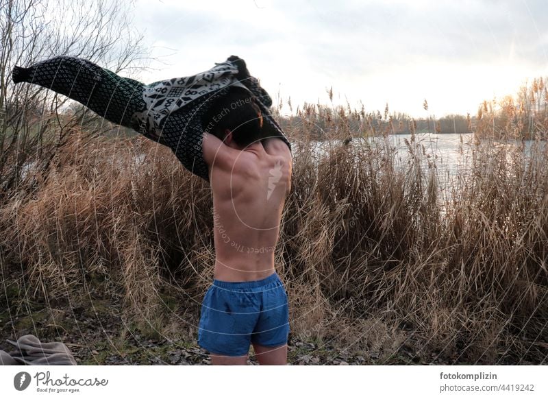 junger Mann in winterlicher Landschaft zieht seinen Pullover aus - macht sich zum Eisbaden bereit Kälte kältegefühl kalt frieren Junger Mann ausziehen