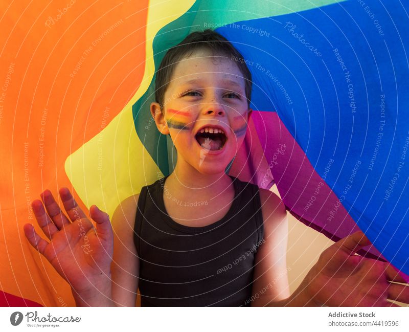 Aufgeregter Junge mit gestreiftem Make-up, der unter der Regenbogenflagge schreit lgbtq Fahne aufgeregt Stolz Solidarität Gleichstellung schreien Konzept