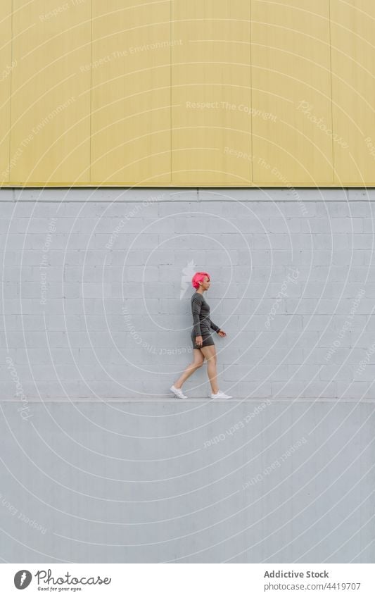 Junger Mann in Sportkleidung geht in der Nähe einer Mauer Frau trendy Straße Wand urban selbstbewusst Außenseite Spaziergang Gebäude Fassade modern grau