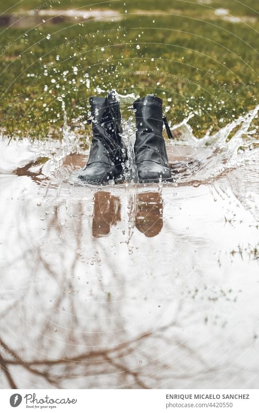 Stiefel, die in eine Pfütze plumpsen und spritzen Kind Spaß Geplätscher Regen nass spielerisch Person Schmutz Schlamm Gummi jung springen platschen Glück