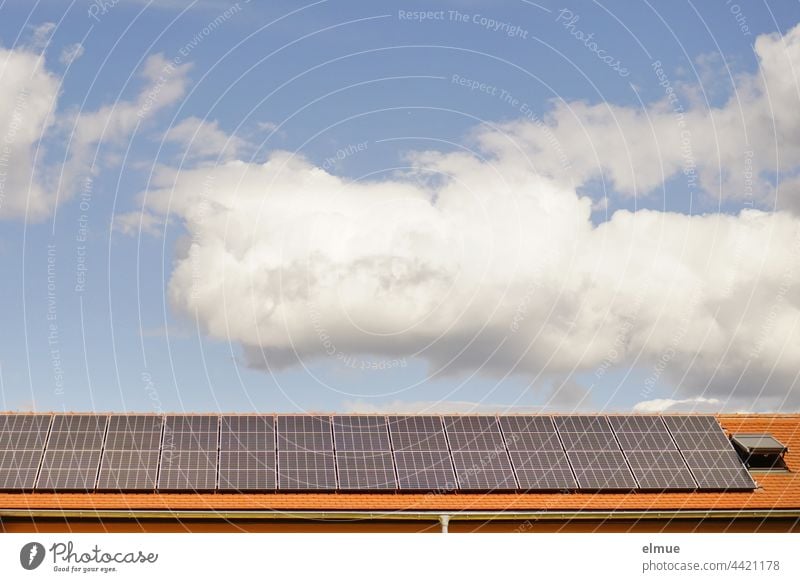 Auf dem roten Ziegeldach, neben einem Dachfenster wurden Sonnenkollektoren installiert / Dekowolken / Ökostrom / Photovoltaikanlage Energiewende Klimawandel