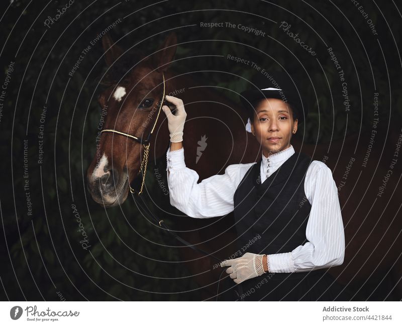 Elegante schwarze Frau mit Pferd im Garten selbstbewusst elegant Jockey Baum Hof historisch Landschaft Starrer Blick nachdenken Tier Afroamerikaner Erwachsener